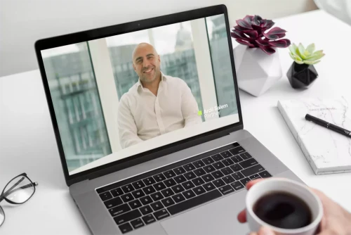 Video of a law firm partner displayed on a laptop screen, with a person holding a coffee cup at a desk watching the video.